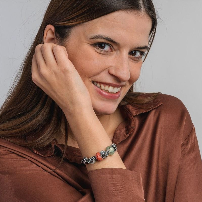 Femme souriante portant un bracelet de breloques Trollbeads avec la perle fleur Fleur Réjouie en arg
