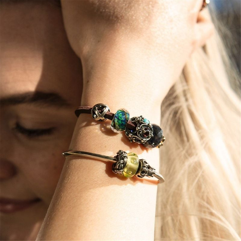Poignet portant un bracelet jonc Trollbeads en argent et un bracelet en cuir avec des breloques et l