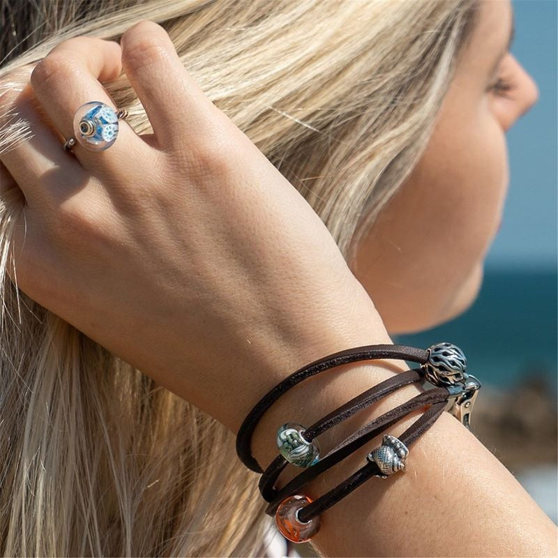 Femme portant un bracelet en cuir Trollbeads avec la perle argentée Conque d’amour et des perles en 