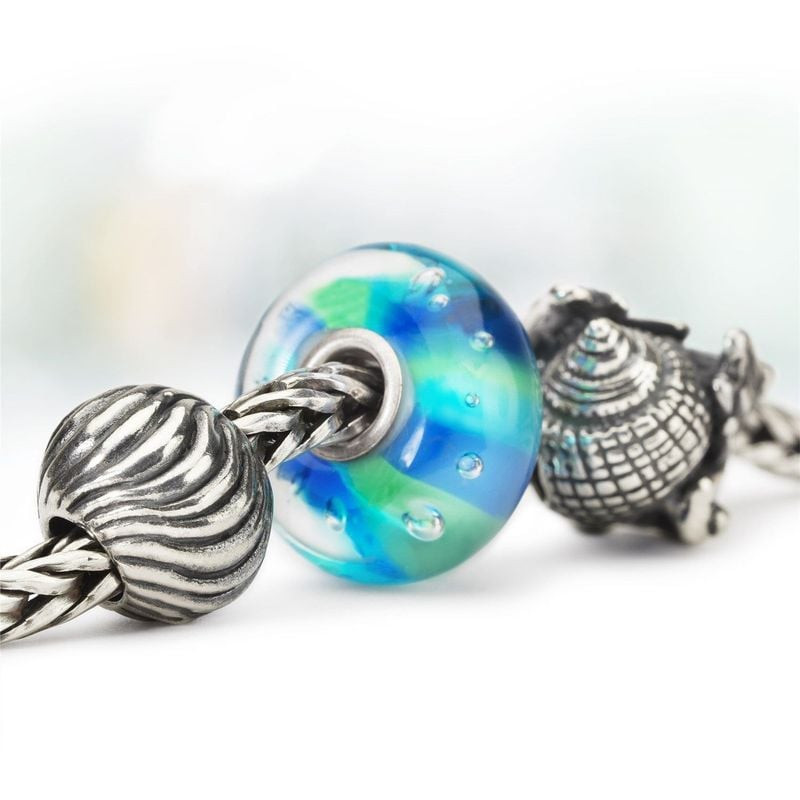 Charme Trollbeads Conque Coquillage Argenté dans un décor marin, évoquant la plage et les vagues.