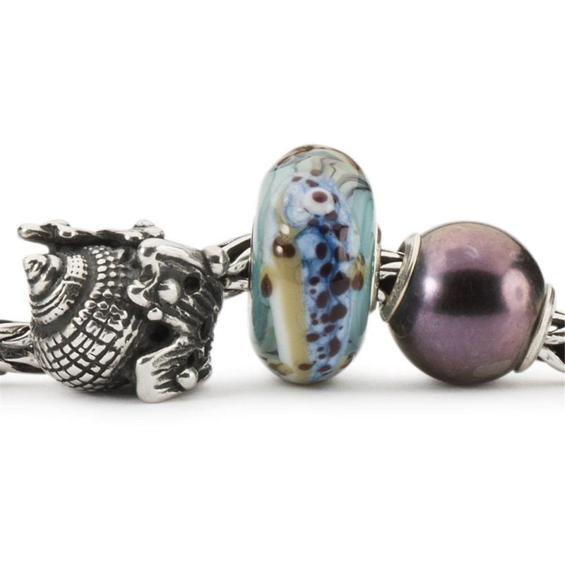 Charme Trollbeads Conque Coquillage Argenté posé sur du sable, évoquant la plage et l'océan.