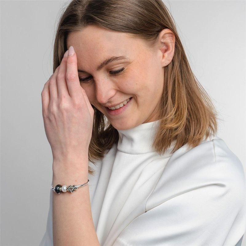 Femme en col roulé blanc souriant avec un bracelet TROLLBEADS en argent et le charm Étoile du berger