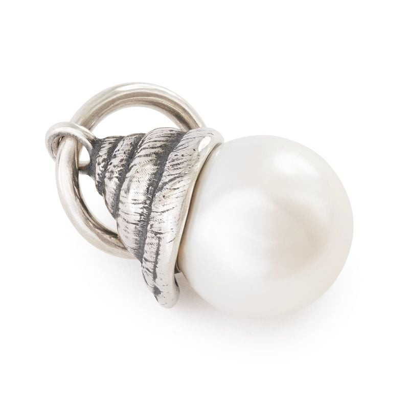 Gros plan du charme coquillage argenté TROLLBEADS enlaçant une perle d'eau douce blanche sur fond bl