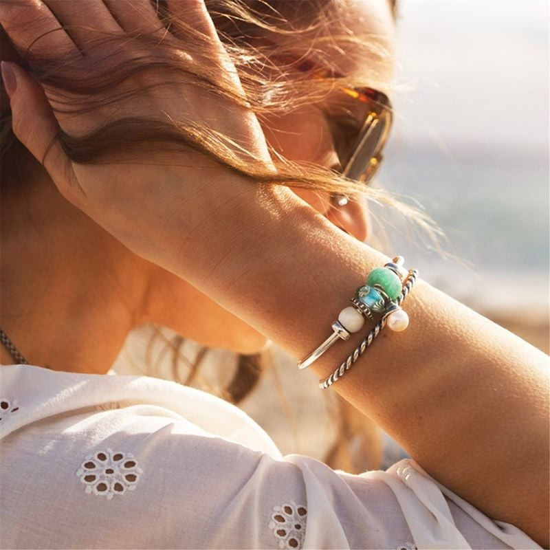 Femme en chemise en lin blanc portant un bracelet de charme océan TROLLBEADS au bord de mer au solei