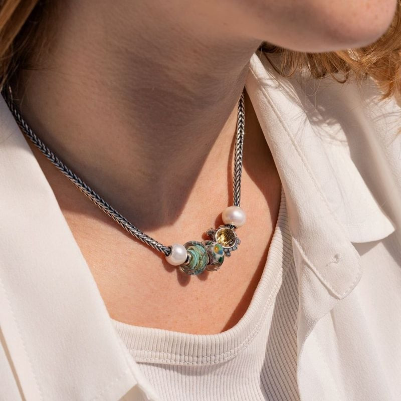 Gros plan sur le cou d'une femme portant un collier avec la perle TROLLBEADS Long Life et d'autres T