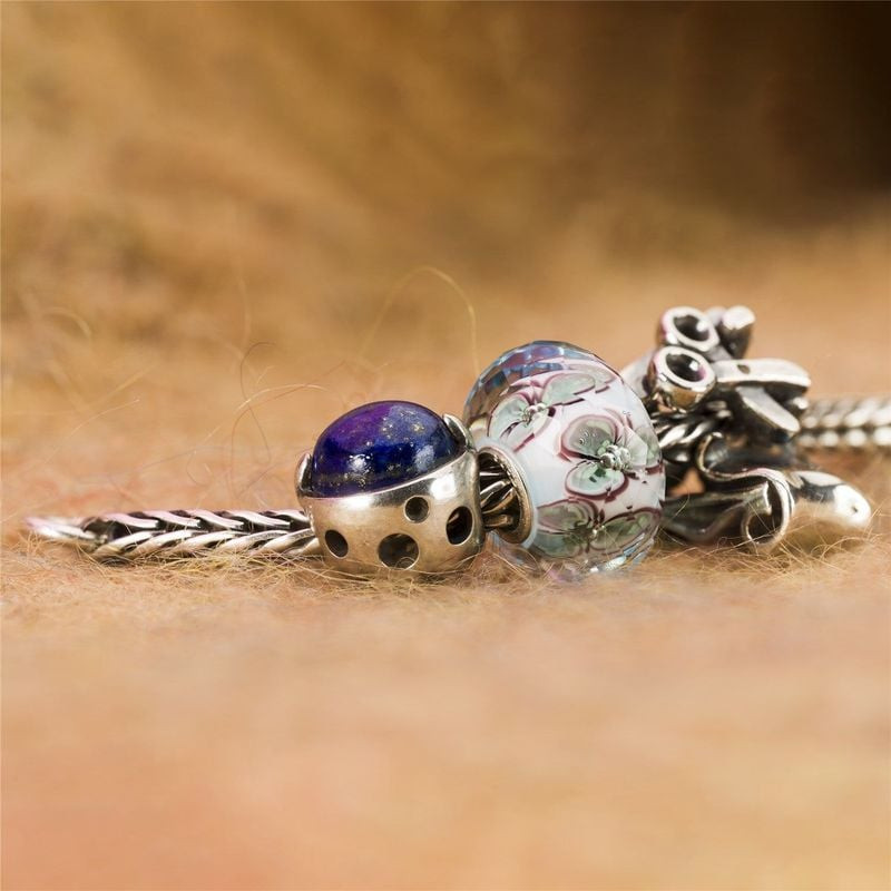 Perle Berceau de la Connaissance TROLLBEADS et charm en verre posés sur une surface douce et texturé