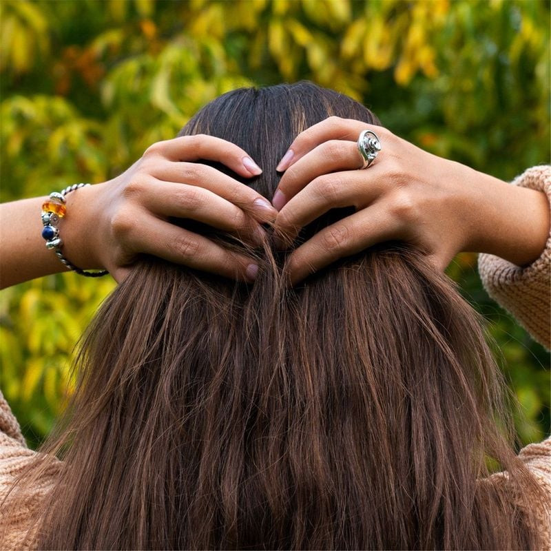 Vue de dos, mains dans les cheveux, dévoilant un bracelet Trollbeads avec la perle Berceau de la Con