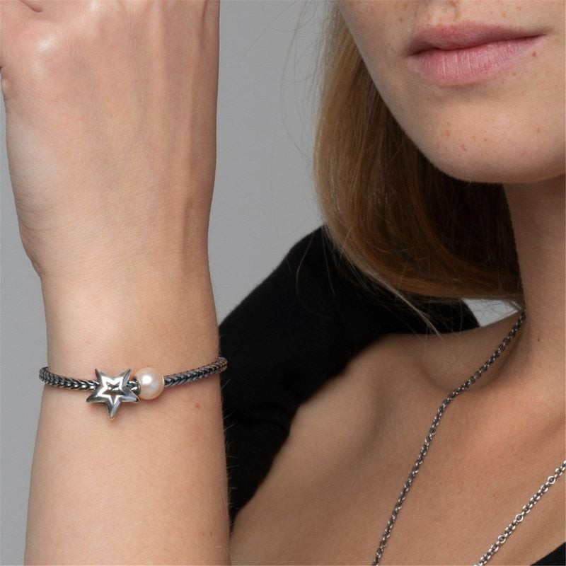 Gros plan sur un poignet portant la perle Rose Trollbeads avec une breloque étoile en argent et une 