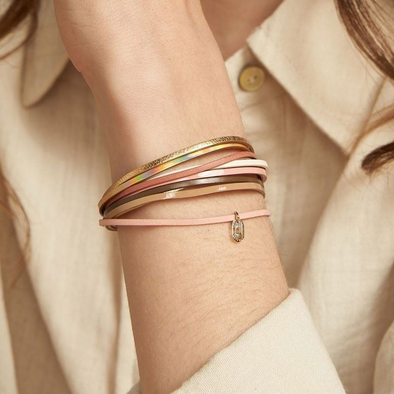 Gros plan d'un poignet portant le bracelet Malicieux Let It Be superposé à un bracelet cordon rose à