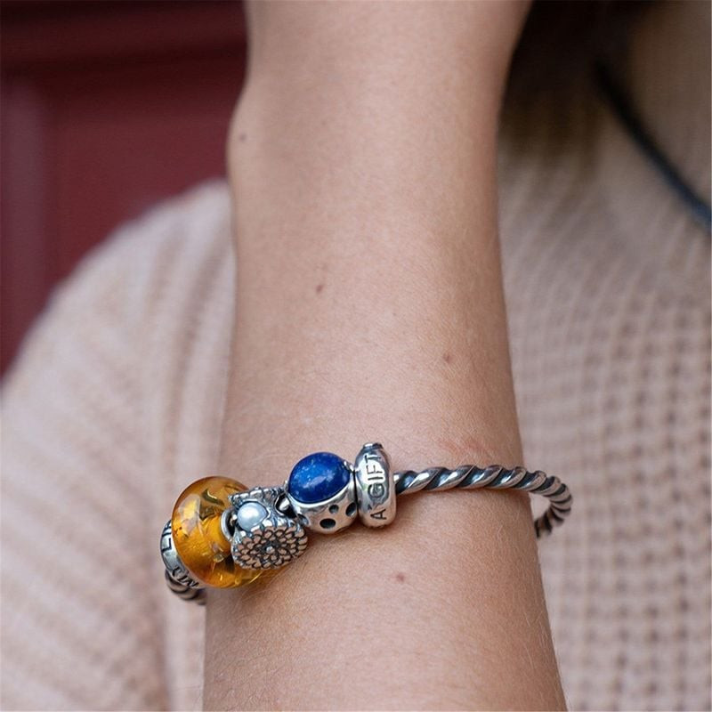 Perle de charme Trollbeads Souci d'octobre Fleur Argenté Blanc portée sur un bracelet