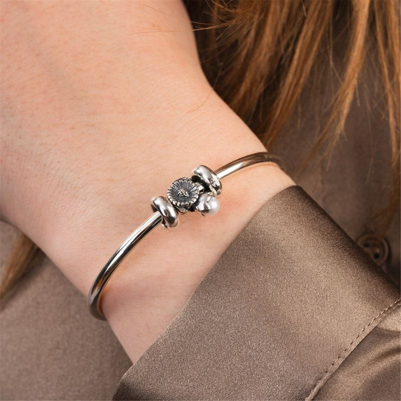 Femme portant un jonc Trollbeads en argent avec le charm Marguerite d'avril et sa perle au poignet