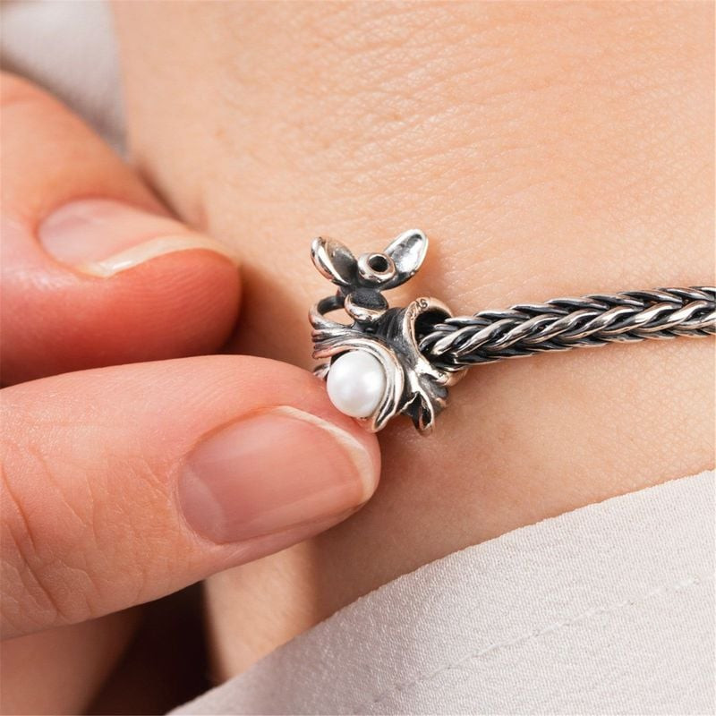 Charme Trollbeads Perce-neige de janvier porté au poignet, doigts effleurant délicatement la perle b
