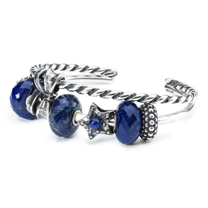 Jonc torsadé Trollbeads en argent orné de perles lapis bleues et d'une perle étoile argent sur fond 