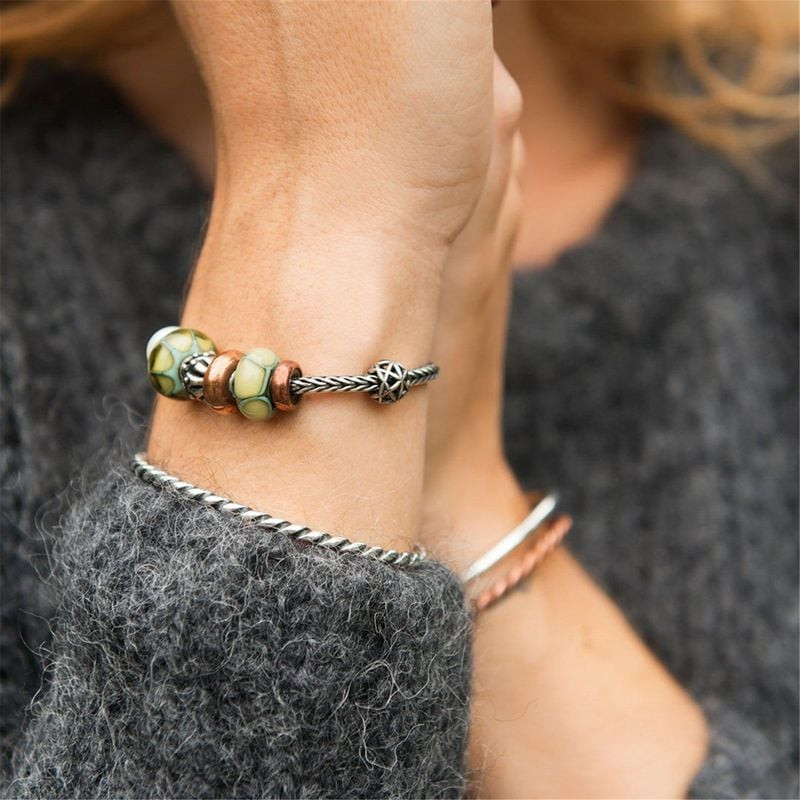 Poignet d'une femme portant le jonc torsadé Trollbeads en argent avec des perles en verre vert sur u