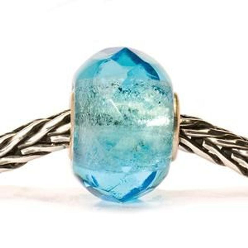 Charm Trollbeads Prisme Verre Turquoise Clair suspendu à un bracelet, reflets turquoise dans une lum