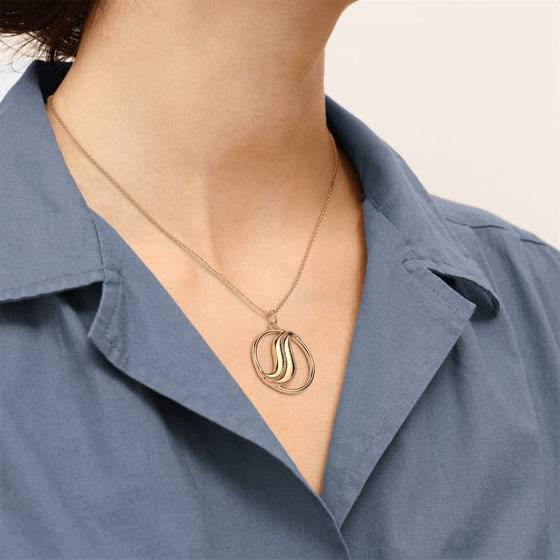 Femme portant le collier Les Georgettes doré Drapé D25MM avec pendentif ajouré sur une chemise bleue