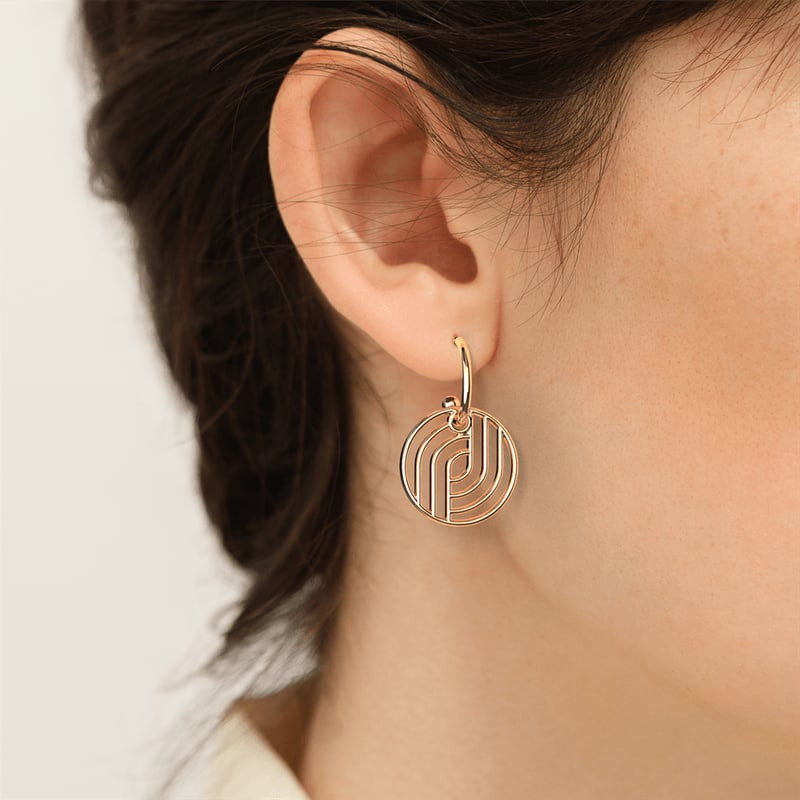 Gros plan d'un mannequin portant une boucle d'oreille Les Georgettes Moderne dorée avec pendentif di