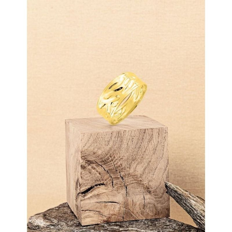 Bague martelée en or jaune présentée sur un bloc de bois rustique, fond beige chaleureux, lumière do